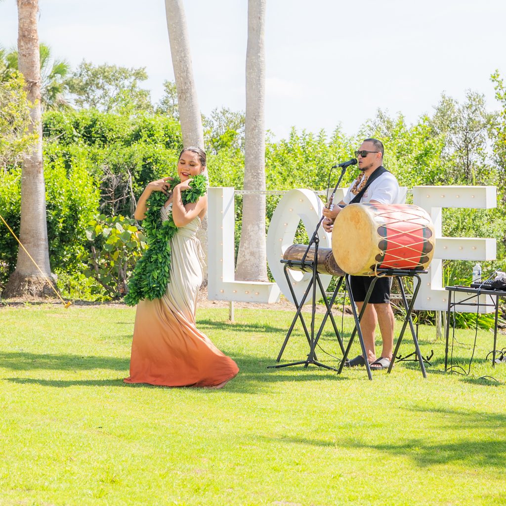 Hula dancer and musician performing on the lawn at Evie’s On the Bay with a large LOVE sign behind them.